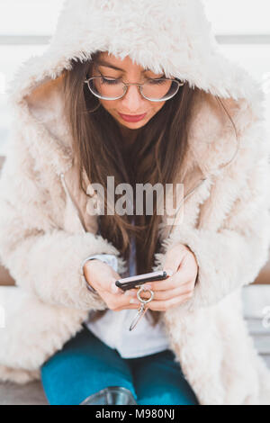 Jeune femme élégante assise sur un banc à l'aide de téléphone cellulaire Banque D'Images