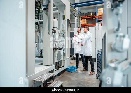 Deux hommes portant des blouses de laboratoire parler en usine Banque D'Images