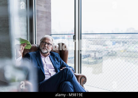 Mature businessman assis dans un fauteuil en cuir holding paper plane Banque D'Images