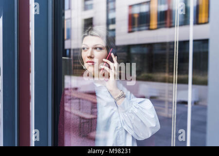 Young woman on cell phone derrière la vitre Banque D'Images