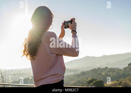 Jeune femme debout sur une colline prenant cell phone photo Banque D'Images