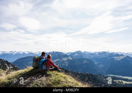 Autriche, Tyrol, young couple sitting in mountainscape looking at view Banque D'Images