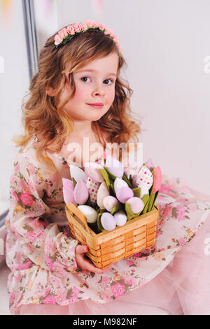 Belle petite fille dans une tenue correcte est assis sur un rebord de fenêtre avec un bouquet de tulipes fleurs sur un arrière-plan de la fenêtre. 8 mars, Pâques, printemps Banque D'Images