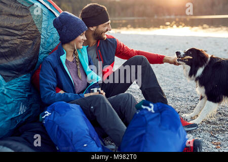 Happy young couple avec chien assis à la tente à Lakeshore Banque D'Images