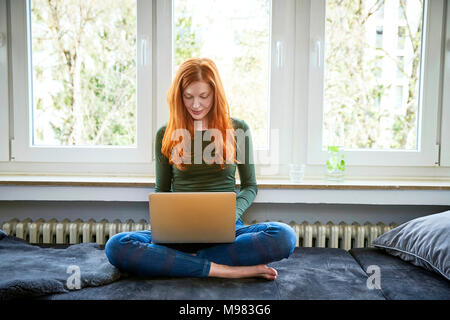 Femme rousse assis en face de la fenêtre à l'aide d'ordinateur portable Banque D'Images