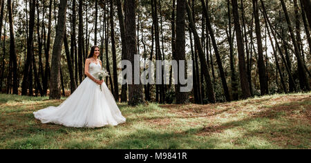 Smiling bride holding bouquet de fleurs en forêt Banque D'Images