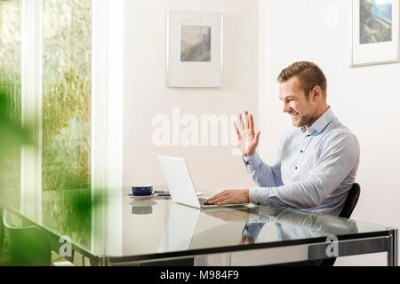 Jeune homme souriant et saluant à son ordinateur portable Banque D'Images