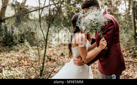 Méconnaissable Bride and Groom kissing in forêt derrière un bouquet de fleurs Banque D'Images