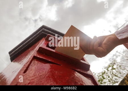 Gros plan sur un homme part mettre une lettre dans une boîte aux lettres rouge. Concept de vintage type de communication. Banque D'Images