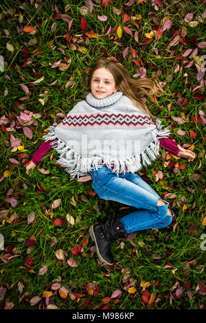 Portrait of smiling girl wearing poncho gisant sur prairie d'automne Banque D'Images