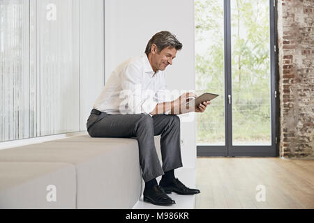 Businessman sitting on bench in modern office using tablet Banque D'Images