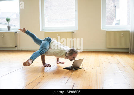 Man doing a handstand in empty room looking at tablet Banque D'Images