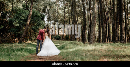 Vue arrière de Bride and Groom kissing in forest Banque D'Images