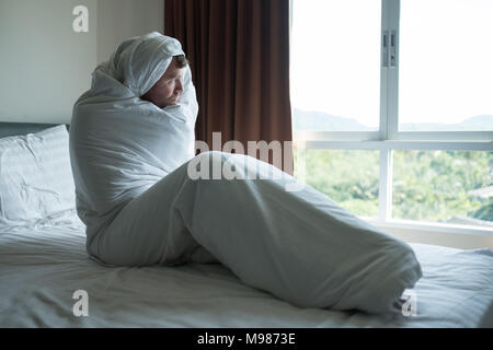 L'homme déprimé assis sur son lit couvert de couverture et à la recherche à fenêtre. Il est enfoncé après un divorce Banque D'Images