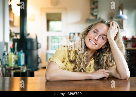 Portrait of smiling blonde woman leaning on table Banque D'Images