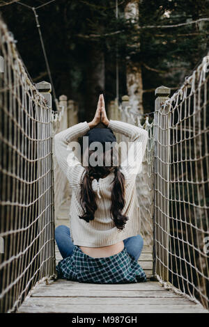 Jeune femme en yoga pose assis sur un pont suspendu Banque D'Images