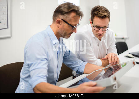 Deux hommes d'examiner panneau solaire sur desk in office Banque D'Images