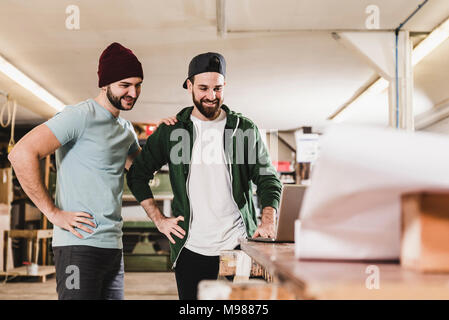 Deux smiling young men looking at laptop in workshop Banque D'Images