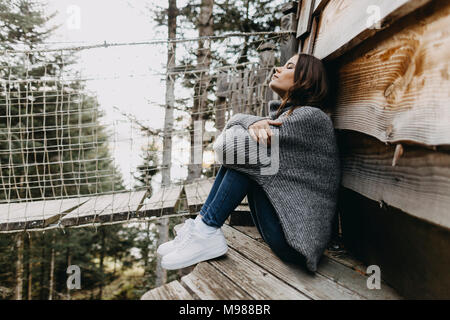 Jeune femme assise à une maison en bois dans la nature se détendre Banque D'Images