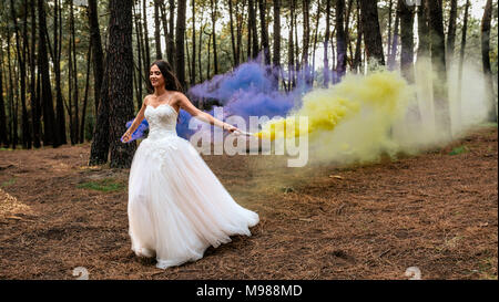 Woman wearing wedding dress in forest holding torches de fumée Banque D'Images