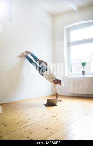 Man doing a handstand in empty room looking at tablet Banque D'Images