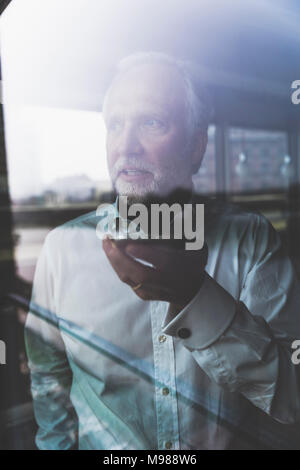 Portrait of mature businessman à la fenêtre using cell phone Banque D'Images