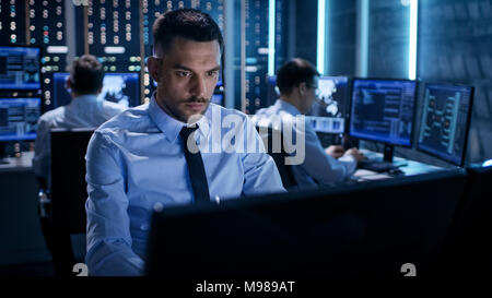 Close-up d'Ingénieur technique de travailler sur son ordinateur avec plusieurs écrans en salle de surveillance. Dans l'arrière-plan ses collègues avec des graphiques Banque D'Images