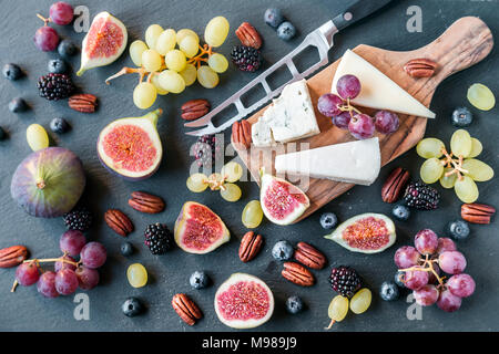Plaque avec du fromage, figues, raisins, bleuets, mûres, noix de pécan, planche à découper, couteau Banque D'Images