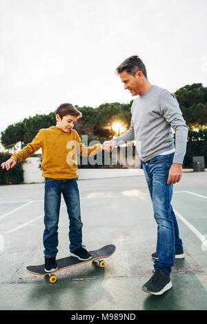 Père aider son riding skateboard Banque D'Images