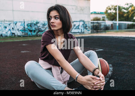 Jeune femme assise avec le basket-ball à l'extérieur sur cour Banque D'Images