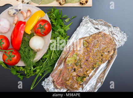 Portrait de la viande marinée sur une plaque près de légumes, le poivre, les oignons, les tomates, l'aneth et le persil sur fond gris Banque D'Images