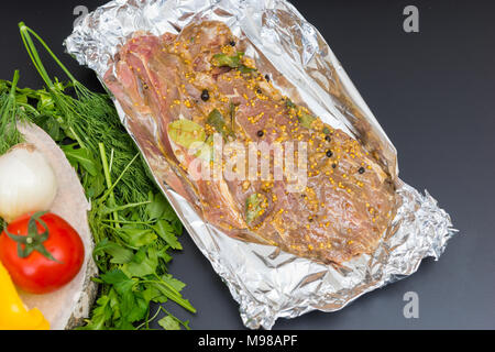 Portrait de la viande marinée sur une plaque près de légumes sur un fond gris Banque D'Images