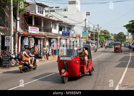 La principale zone touristique street road à Hikkaduwa, Sri Lanka sur une journée ensoleillée avec ciel bleu, Tuk Tuks et les scooters. Banque D'Images