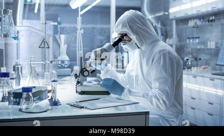Dans un laboratoire de recherche de haut niveau scientifique dans une combinaison de Petri examine au microscope. Banque D'Images