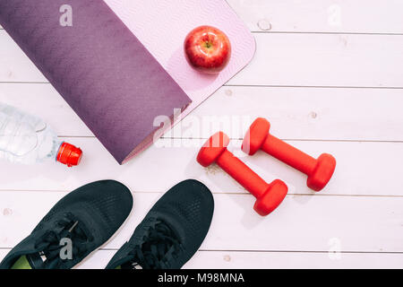 Tapis de Yoga, les chaussures de sport, des haltères et une bouteille d'eau sur fond bleu. Concept de vie sain, le sport et l'alimentation. Les équipements de sport. Copy space Banque D'Images