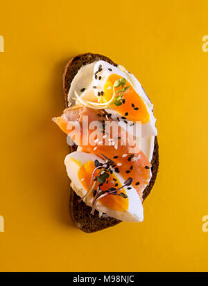 Petit-déjeuner sain des toasts. Farine de seigle tranches de pain avec du fromage à la crème, les oeufs, le saumon, Sesam et microgreen. Concept de l'alimentation propre. Fond jaune. Banque D'Images