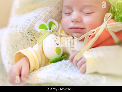 Portrait of a cute little baby garçon endormi dans son lit à la maison avec des oeufs décorés-bunny toy, symbole traditionnel de Pâques, joyeuses Pâques, vacances de printemps Banque D'Images