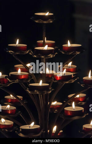 Pyramide de bougies votives dans des conteneurs métalliques rouges dans une église sombre Banque D'Images