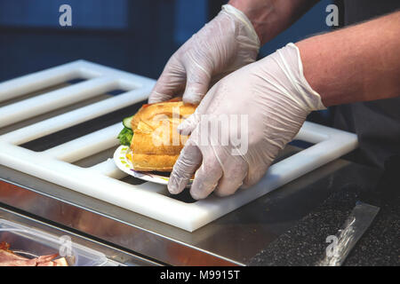 Faire cuire dans des gants jetables met un sandwich sur une plaque à usage unique Banque D'Images