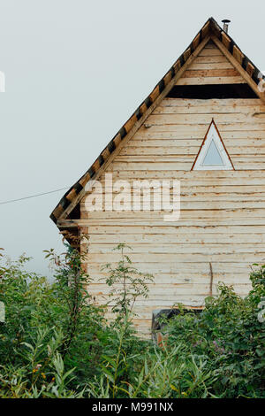 Voyage en bois maison avec une fenêtre triangulaire dans la taïga de l'herbe. Banque D'Images