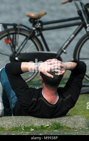 Un homme est relaxant au bord de l'eau avec son vélo à l'avant-plan Banque D'Images