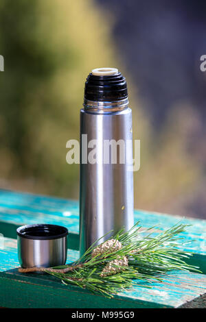 Thermos avec du thé sur un banc avec des pommes de pin Banque D'Images