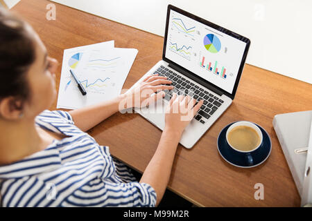Jeune femme travaillant sur des tableaux sur son ordinateur portable à la maison Banque D'Images