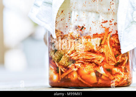 Gros plan du pot de verre d'emballage de produits frais faits maison poivre épicé fermenté chou kimchi coréen avec jus de légumes, rouge foncé, serviette Banque D'Images