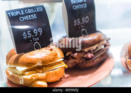 Sandwich bagel au fromage triple signe avec des prix sur l'écran avec du pain, de la viande en magasin, boutique, restauration rapide sur la plaque Banque D'Images