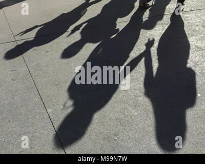 De longues ombres de personnes tenant la main et marcher le long du trottoir dans l'après-midi Banque D'Images