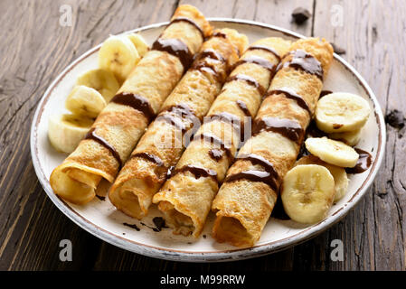 Délicieux rouleau crêpe avec des tranches de banane et sauce au chocolat sur fond de bois. Vue rapprochée Banque D'Images