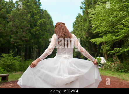 Femme en blanc mariage robe lacée holding bouquet dans une forêt Banque D'Images