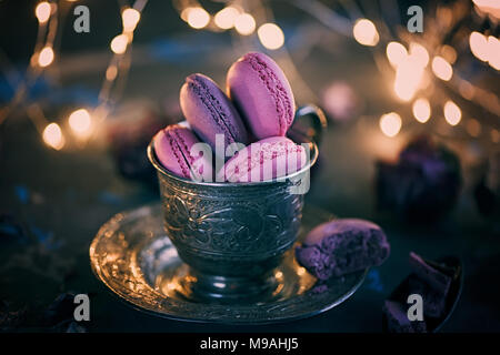 Des petits macarons sur une coupe de métal de l'argent avec de l'effet bokeh voyants sur le fond en bois. Focus sélectif. Spase copie Banque D'Images