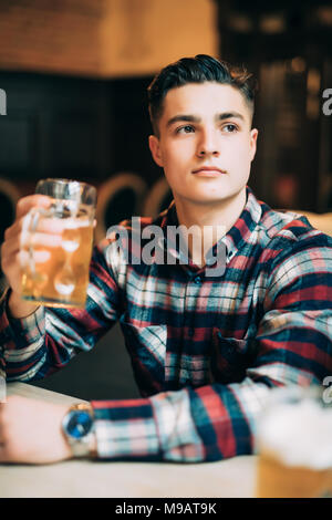 L'homme dans la bière pub. Cheerful young man holding a beer mug et smiling while sitting in bar Banque D'Images